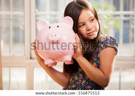 Pretty little girl shaking her piggy bank and trying to figure out how much money she has saved