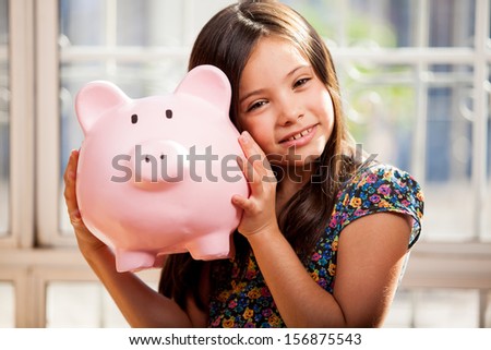 Beautiful little brunette shaking a piggy bank and wondering how much money is inside