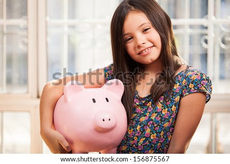 Cute little girl learning how to save money with a piggy bank and smiling