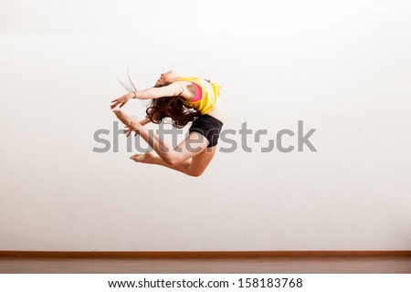 Gorgeous jazz dancer in the middle of a jump during a dance performance in a studio