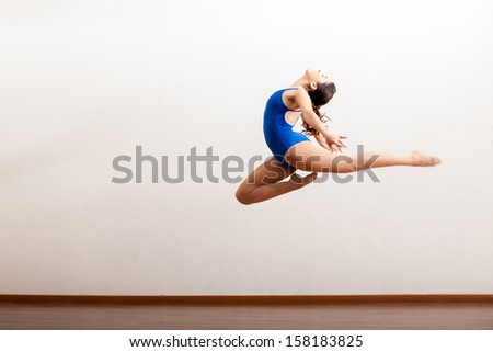 Cute female dancer in a leotard practicing a big jump of her dance routine in a studio
