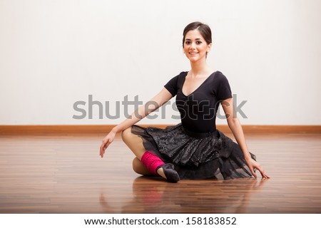 Cute happy ballet dancer sitting on the dance floor in the middle of a dance routine