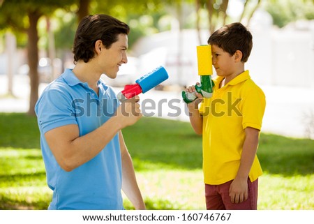 Portrait of a young Latin father and his son ready to play with water guns at a park