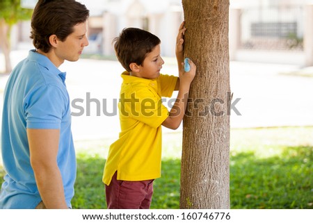 Young father and son writing the boy\'s name with chalk on a tree