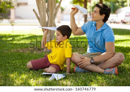 Young Latin dad and his son folding some paper planes and having fun together at a park