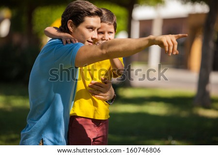 Young Latin father pointing and showing something to his cute son outdoors