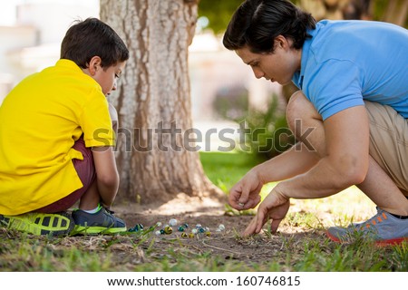 Handsome young dad spending some time with his son and playing marbles at a park