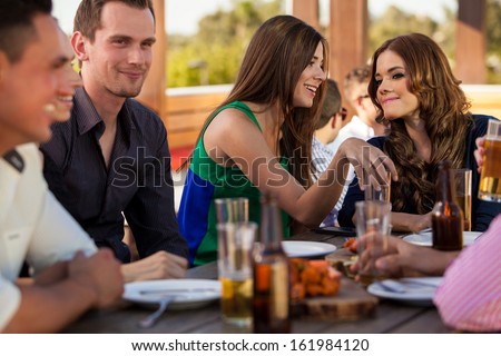 Young Female Friends Talking To Each Other While Hanging Out With A Bunch Of Friends At A Restaurant