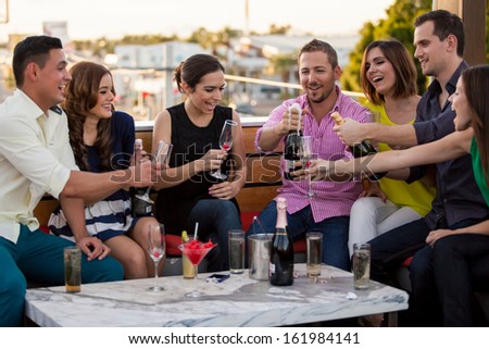 Large group of friends celebrating and popping a bottle of champagne