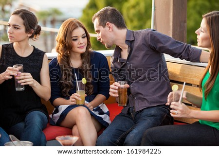 Young Hispanic couple talking and flirting while hanging out with a bunch of friends