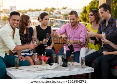 Group Of Young Adults Celebrating With Champagne And Having Fun At A Bar Outdoors