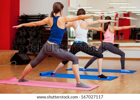 Group of young women practicing the warrior yoga pose during a class in a gym