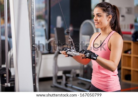 Pretty young woman using a pulley to tone her muscles in a gym