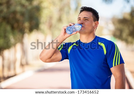 Athletic young man drinking water and taking a break from running on a sunny day