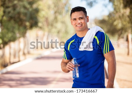 Young handsome athlete resting and drinking water after a run in a running track