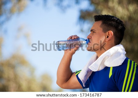 Strong young man drinking water and cooling off after a run on a sunny day
