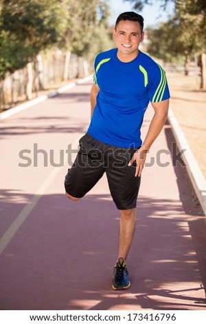 Young male runner stretching his legs as part of his training at the running track