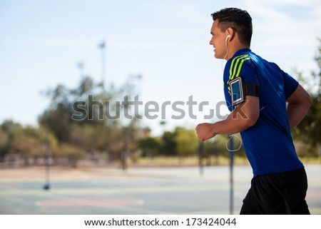 Young Fit Guy Wearing His Cell Phone With And Armband And Running On A Sunny Day