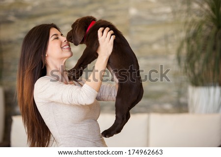 Beautiful Hispanic Young Woman Lifting Up Her Puppy And Giving Him A Kiss