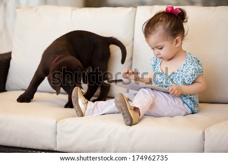 Pretty little girl using a tablet computer while her puppy keeps her company