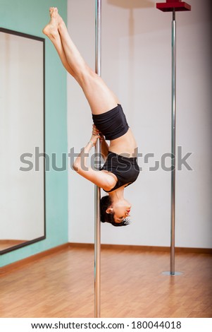 Young pole dancing student working out and hanging from a pole during a pole fitness class