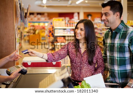 Beautiful young brunette and her boyfriend buying some groceries at the supermarket and paying with a credit card