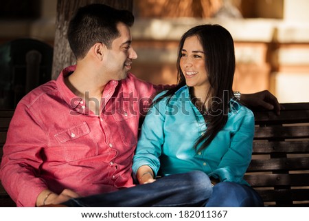 Beautiful young couple relaxing in a park bench and smiling at each other