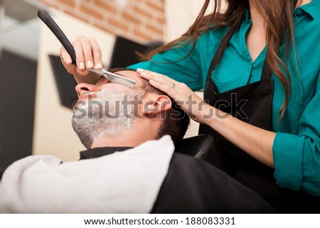 Low angle view of a female barber shaving a man\'s beard in a barber shop