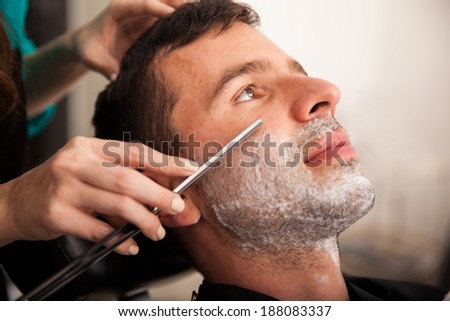 Portrait of a young man getting his beard shaved by a lady barber