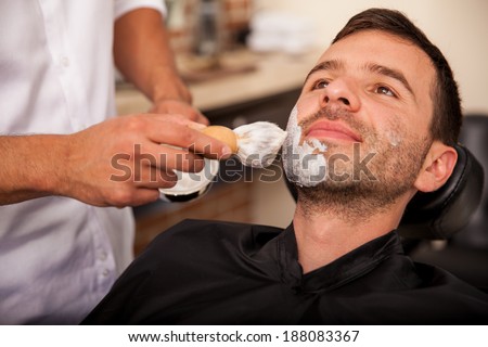 Closeup of a barber putting some shaving cream on a client\'s face before giving him a shave