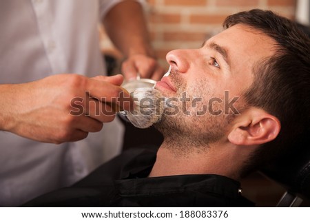 Profile view of a barber using a brush to put some shaving cream on a client\'s face