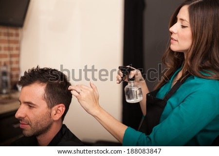 Cute young hairstylist spraying some water on a client\'s hair in a hair salon