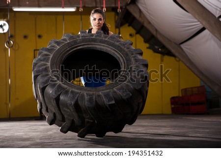 Gorgeous young woman working out with a big tire in a cross-training gym