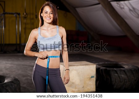 Beautiful Hispanic woman measuring her waist to check her progress at a cross-training gym