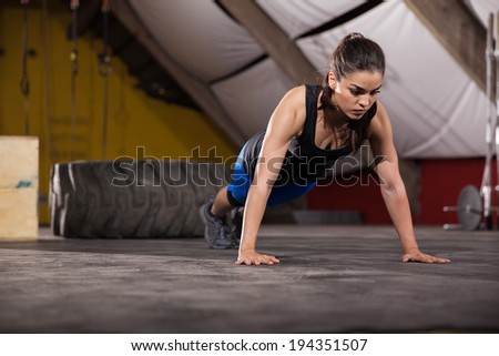 Athletic Latin woman doing push ups with extreme determination in a cross-training gym