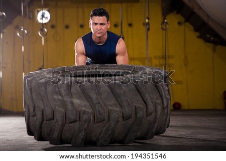 Athletic young man lifting a big tire as part of the workout of the day in a cross-training gym