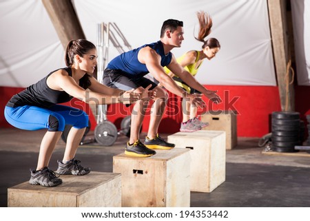 Group of athletic people jumpin over some boxes in a cross-training gym