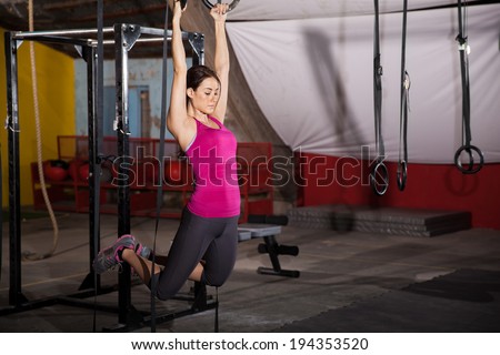 Pretty Hispanic woman working out in the gymnastic rings in a cross-training gym