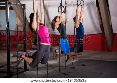 Group of three people pulling their weight up in the gymnastic rings in a cross-training gym