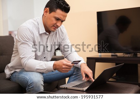Latin young man shopping online using his credit card and laptop computer