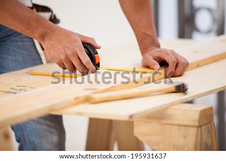 Closeup of a contractor using a tape measure to mark down some dimensions on a wood board