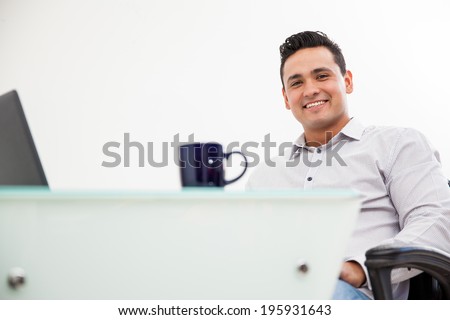 Portrait of a young Latin man working at his office and drinking coffee