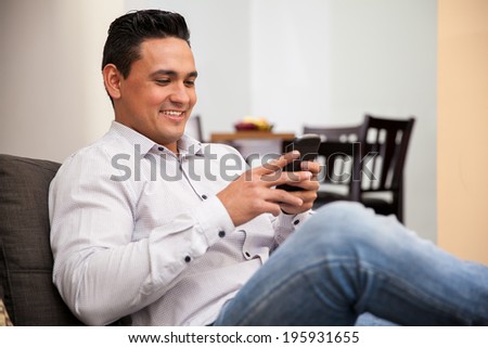 Happy young man social networking and texting with his smart phone at home