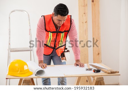 Attractive contractor wearing a vest and looking at the floor plan of a house