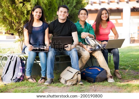 Group of high school students using all kinds of devices while hanging out