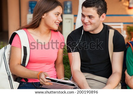 Cute couple of high school students flirting with each other and listening to music from a tablet computer