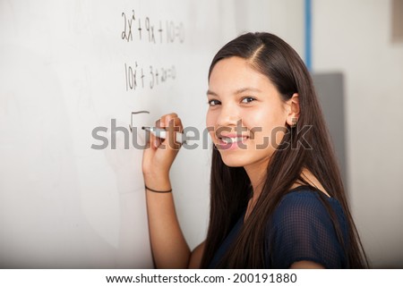 Beautiful Hispanic student writing on a white board at school and smiling