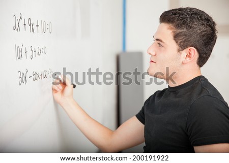 Handsome young high schooler solving some algebra equations on a white board