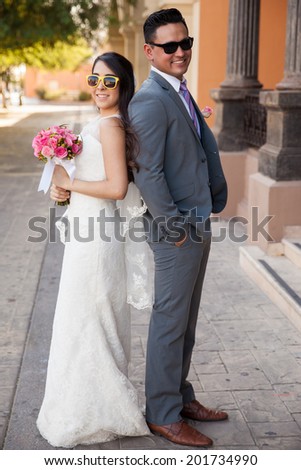 Full length portrait of a bride and groom back to back wearing sunglasses outside a church