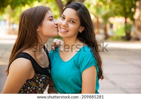 Beautiful Hispanic teen kissing her best friend in the cheek and smiling